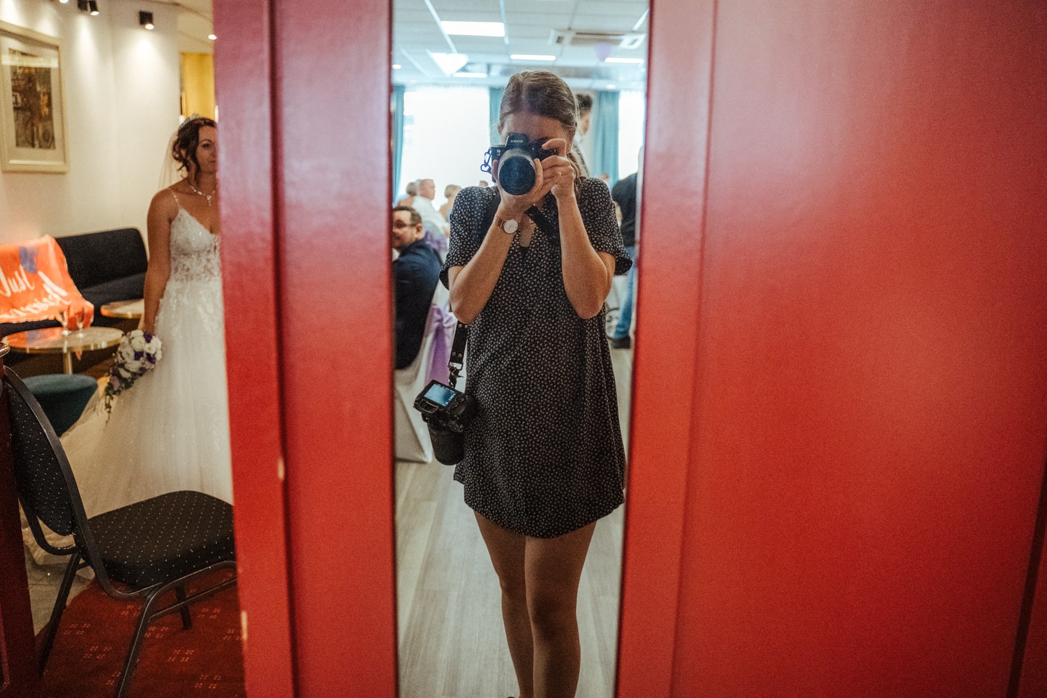Hochzeitsfotografin Mirjam Beitz mit zwei professionellen Kameras mit der Braut im Hintergrund